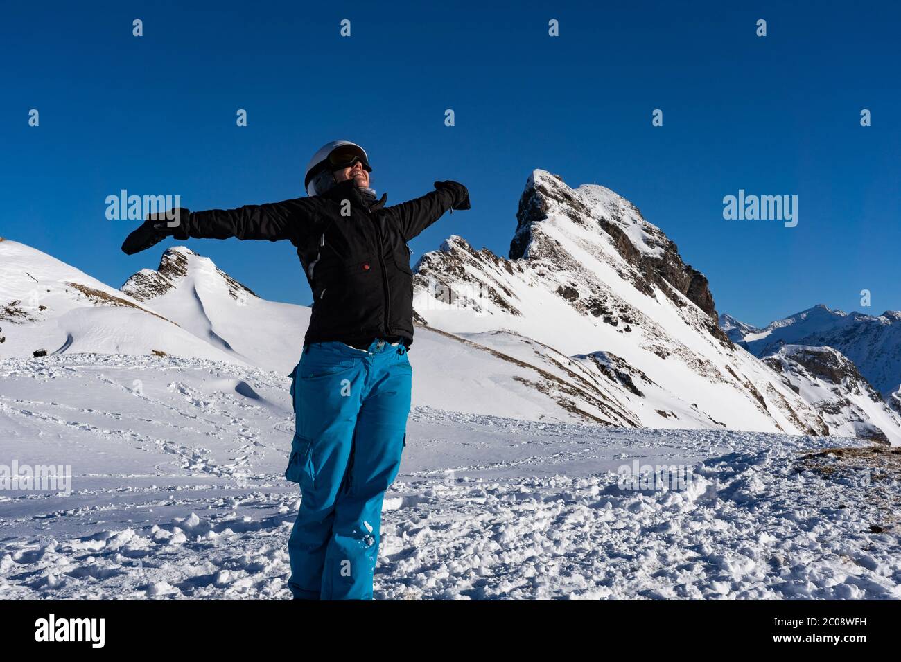 Fille profitant de soleil d'hiver avec des bras ouverts au sommet de la chaîne de montagne. Snowboardeur en fin d'après-midi dans les alpes suisses en hiver. Concept pour expr Banque D'Images