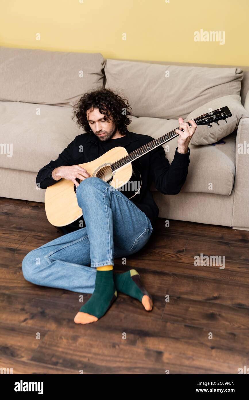 Beau homme jouant de la guitare acoustique au sol dans le salon Banque D'Images