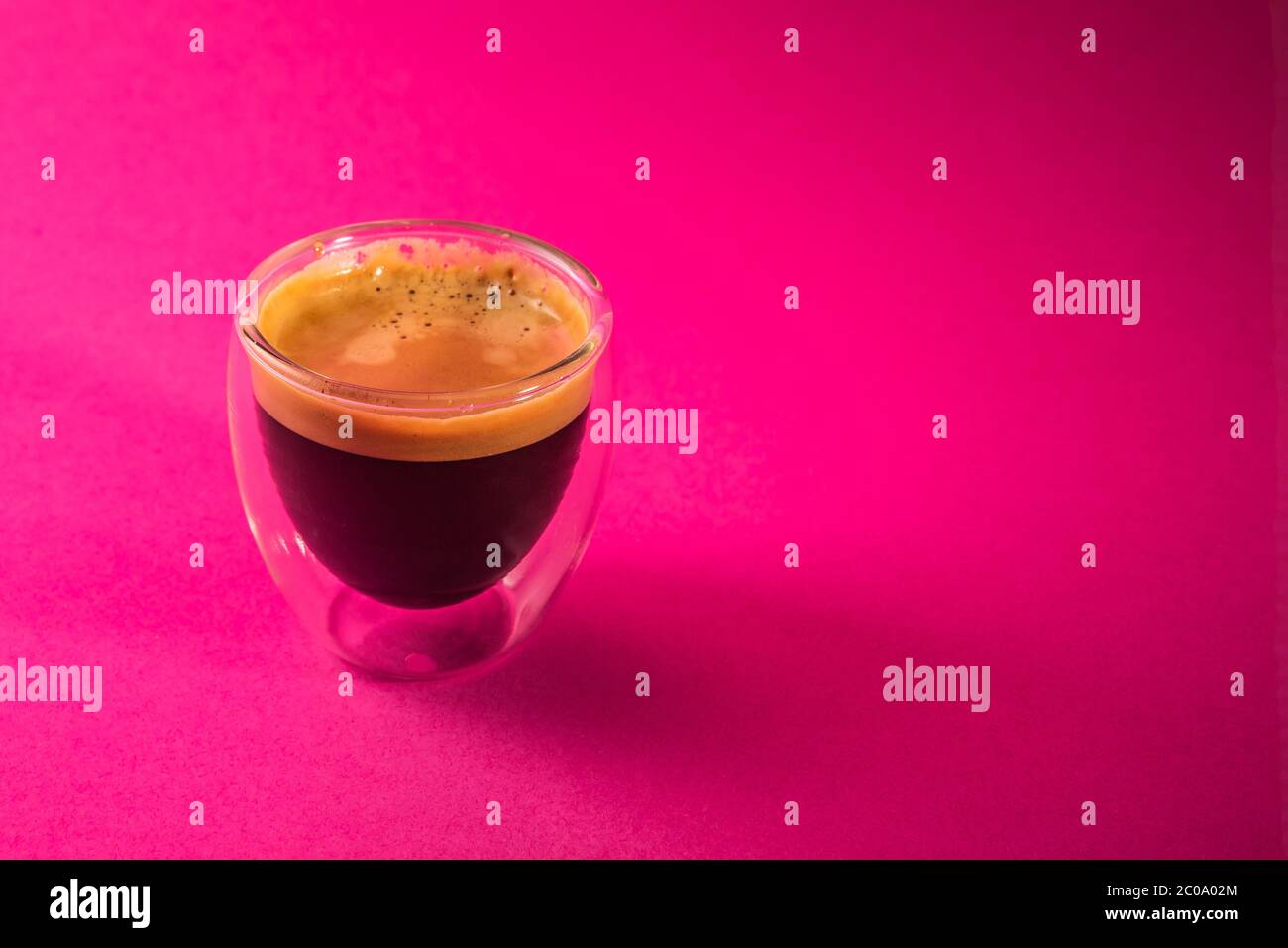 Espresso crémeux fraîchement préparé dans une tasse de café en verre isolée sur fond rose, en gros plan avec l'espace de copie Banque D'Images