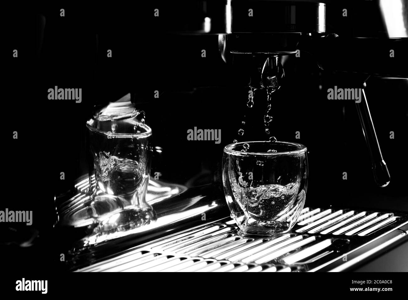 Gros plan de gouttes d'eau chaude qui s'écoulant dans une tasse à espresso transparente provenant d'une machine à café manuelle pour le préchauffage, monochrome, avec espace de copie Banque D'Images