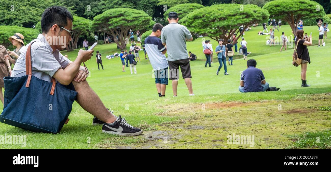 Jeune japonais avec smartphone au jardin Shinjuku Gyoen pendant l'été, Tokyo, Japon. Banque D'Images
