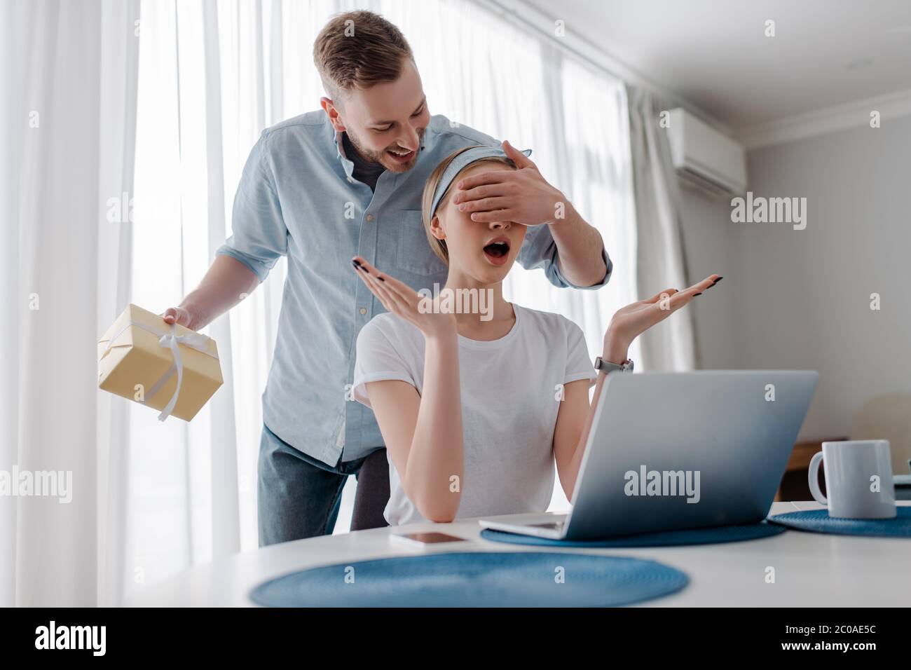 beau homme couvrant les yeux de petite amie surprise tout en tenant présent Banque D'Images