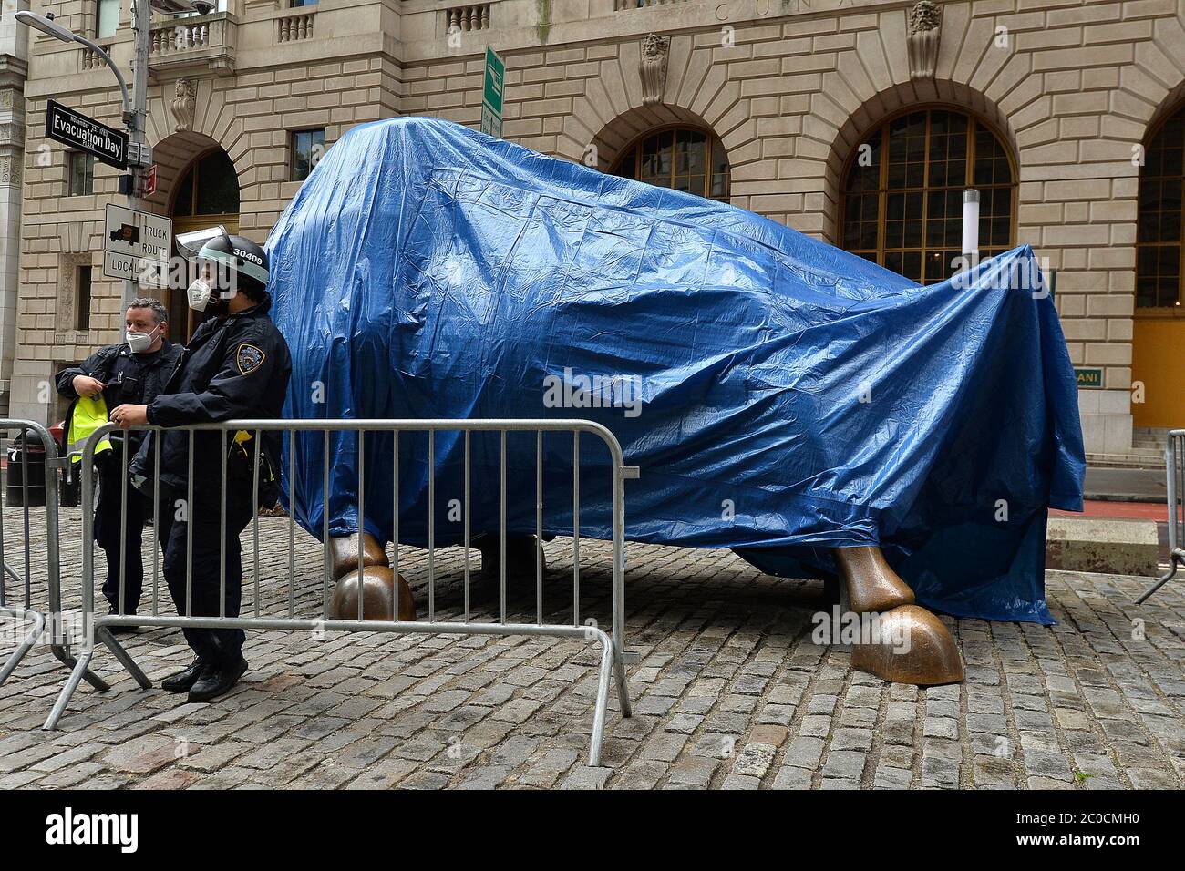 New York, États-Unis. 11 juin 2020. Un officier du NYPD, portant un masque facial à l'époque de COVID-19 et un casque anti-émeute, se tient à côté de « Charging Bull » par l'artiste Arturo Di Modica, couvert d'une bâche bleue pour éviter tout dommage, les manifestants ayant défilé plus tôt dans la journée dans le quartier financier de New York, NY, 11 juin 2020. Les manifestants ont renversé de la peinture rouge le long de Broadway près de la statue de bronze, mais elle n'a pas été endommagée. (Anthony Behar/Sipa USA) crédit: SIPA USA/Alay Live News Banque D'Images