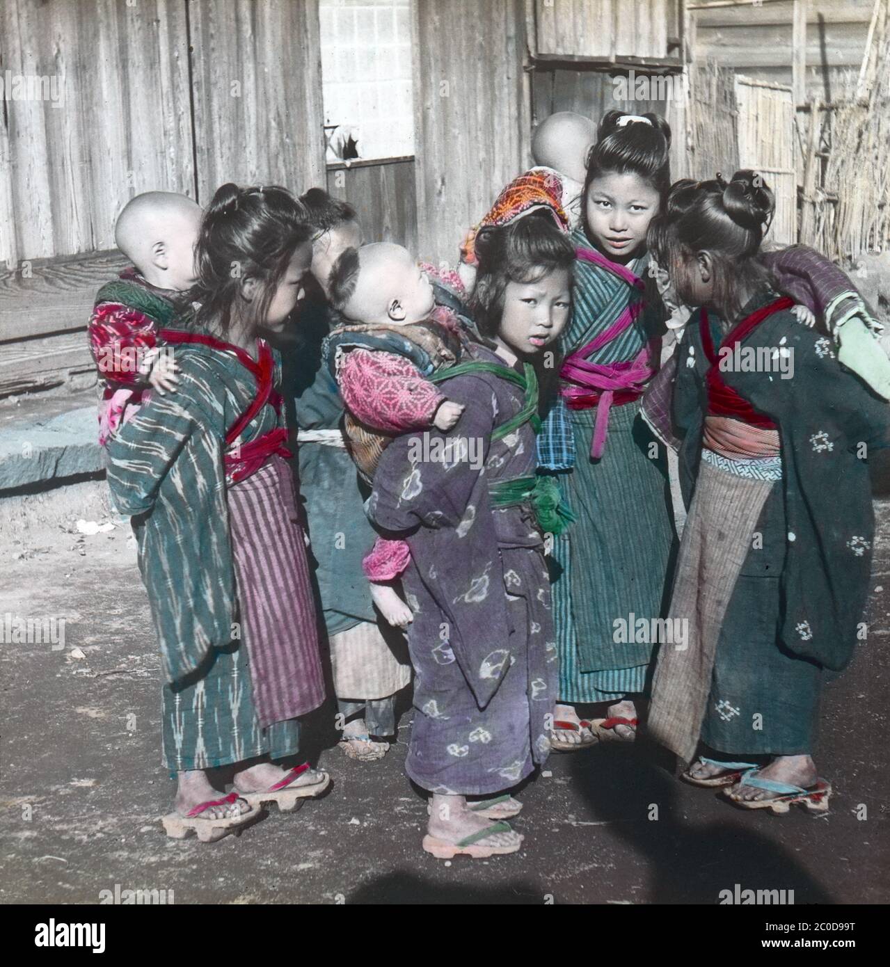 [ 1900s Japon - jeunes aides infirmières japonaises ] — UN groupe de komori sur une route de campagne au début des années 1900. Les Komori étaient de jeunes filles de familles pauvres qui ont été embauchées chaque année pour aider les mères de classe moyenne et supérieure à prendre soin de leur bébé. En plus de transporter le bébé, le komori aiderait également un peu le travail de ménage. Komori a reçu de la nourriture, de l'hébergement, des vêtements et parfois de l'argent. diapositive en verre vintage du xxe siècle. Banque D'Images