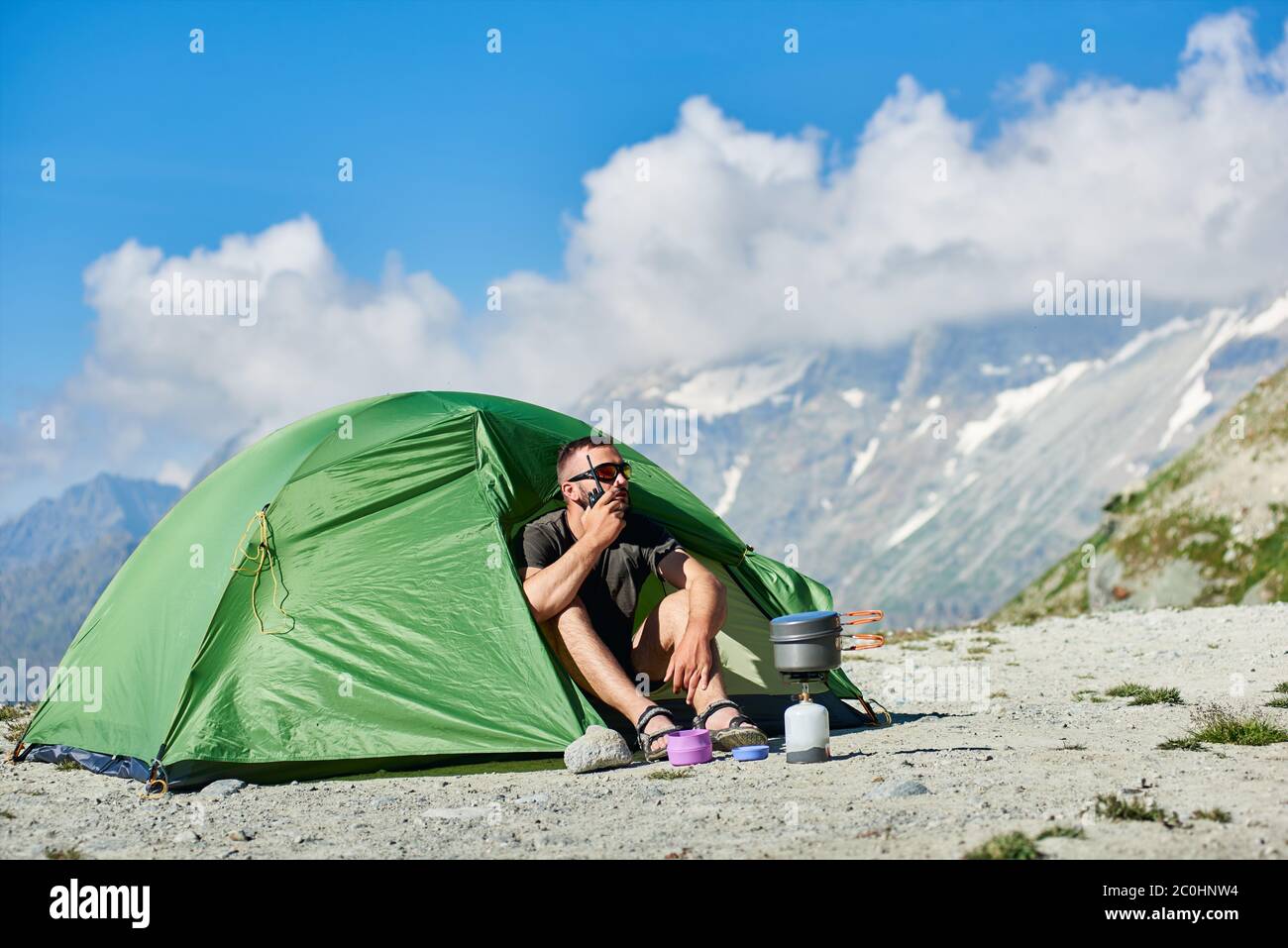 Homme touriste assis à l'intérieur de la tente du camp et utilisant le  walkie-talkie. Homme voyageur avec radio à la main se reposant dans une  tente touristique avec montagnes et ciel bleu