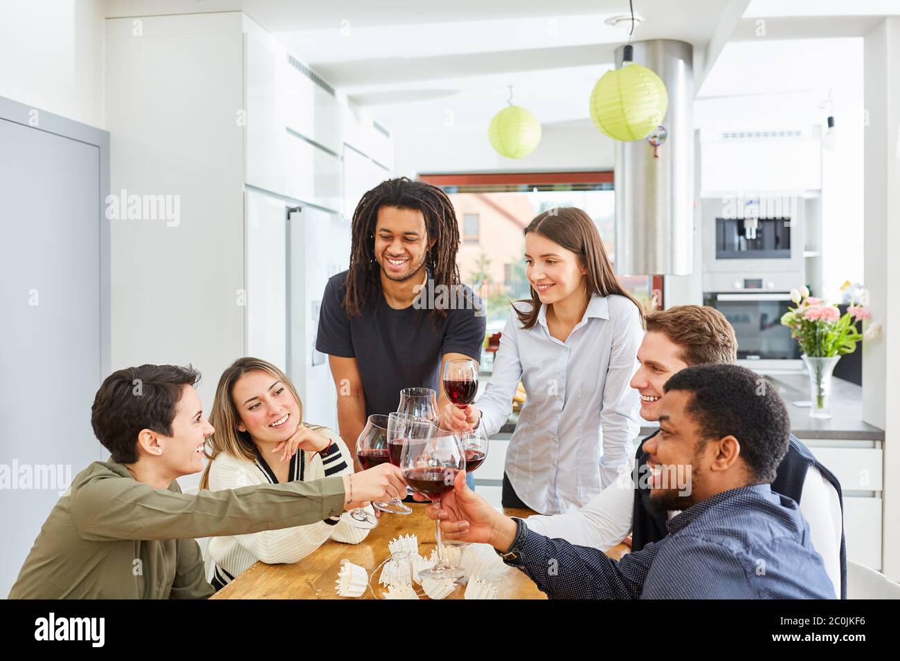 Des amis heureux toastent avec un verre de vin rouge dans la cuisine et fêtent Banque D'Images