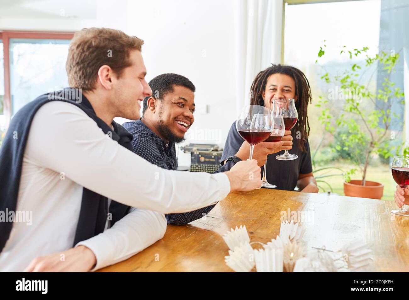 Groupe d'hommes comme amis qui boivent et trinquer du vin à la maison dans une cuisine commune Banque D'Images