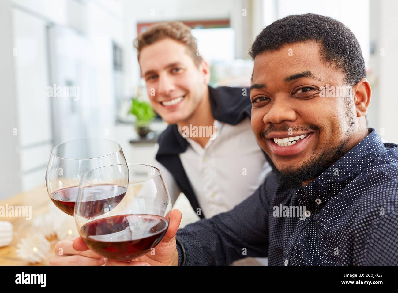 Les amis s'assoient à la table à la maison avec un verre de vin rouge et se rôtir Banque D'Images