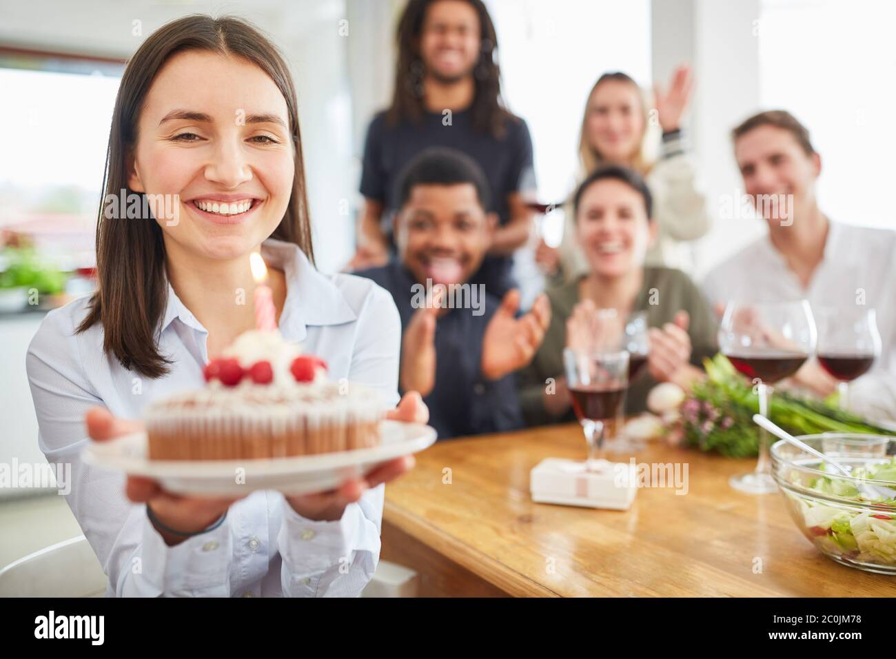 Une jeune femme donne un gâteau avec une bougie pour l'anniversaire à ses amis dans la cuisine Banque D'Images