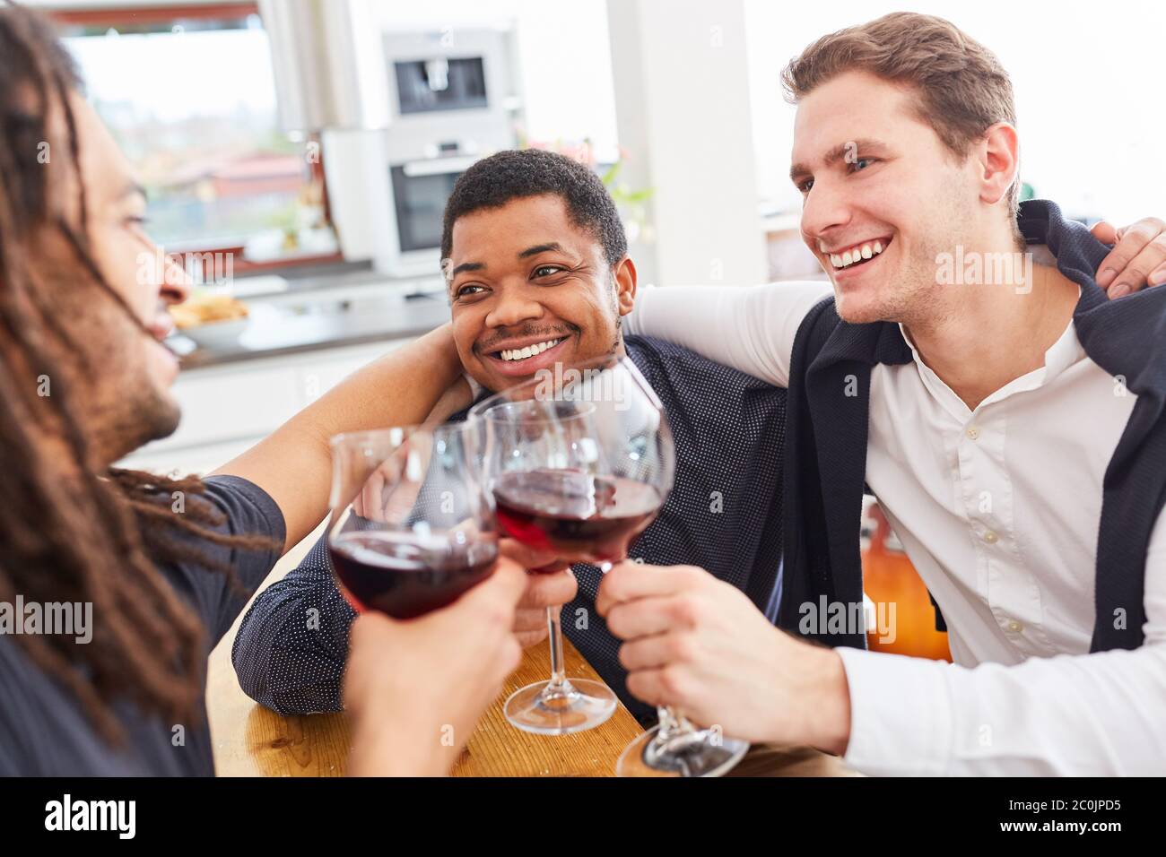 Les hommes comme amis à la maison se câlin les uns les autres tout en buvant du vin et des verres de clin d'œil avec un verre Banque D'Images