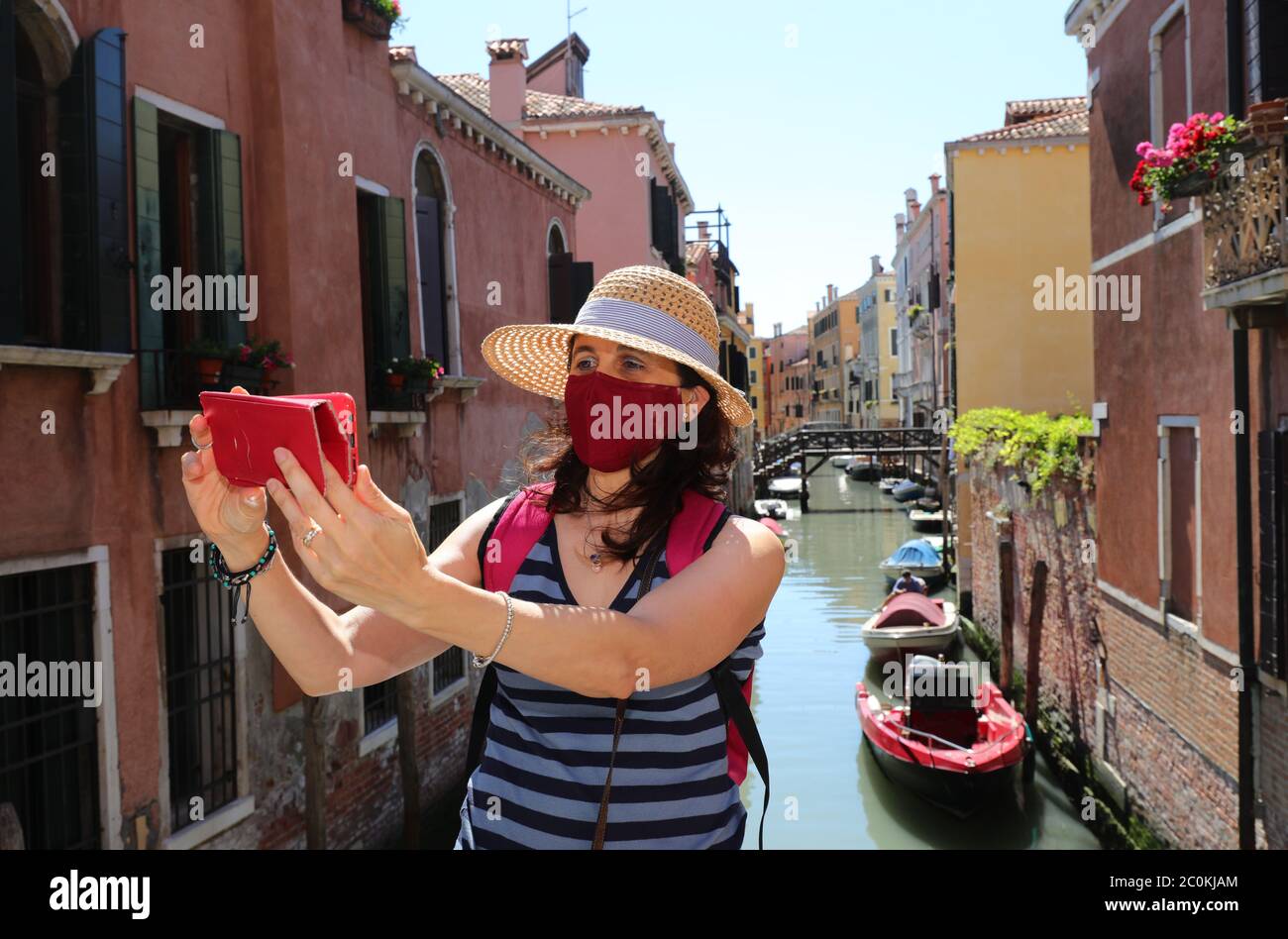 Femme avec masque chirurgical et chapeau de paille prend une photo avec un téléphone portable sur le pont au-dessus de la voie navigable à Venise pendant la pandémie du virus Corona Banque D'Images