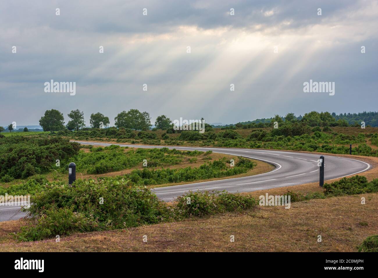 Route sinueuse de campagne avec ciel sombre et puits de lumière du soleil se faisant briller, New Forest, Hampshire, Royaume-Uni Banque D'Images