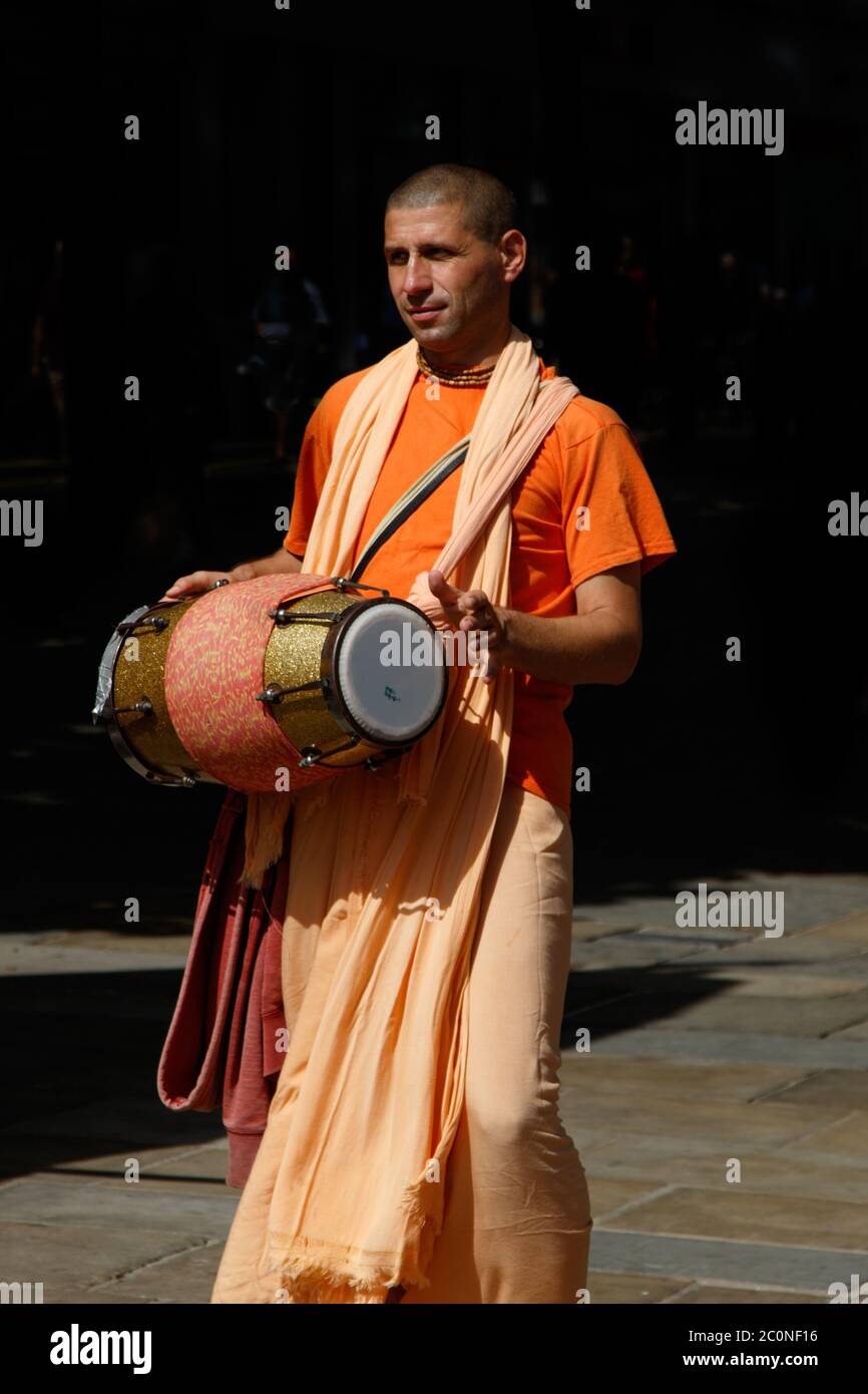 Homme Hare Krishna portant des robes orange et marchant dans une rue de ville jouant un tambour, York, North Yorkshire, Angleterre, Royaume-Uni. Banque D'Images