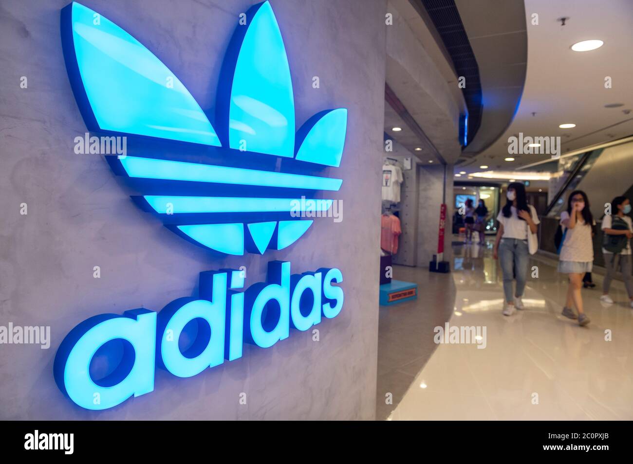 Les acheteurs portant des masques faciaux se promène devant le logo Adidas, une marque multinationale allemande de vêtements de sport, dans un centre commercial de Hong Kong Banque D'Images