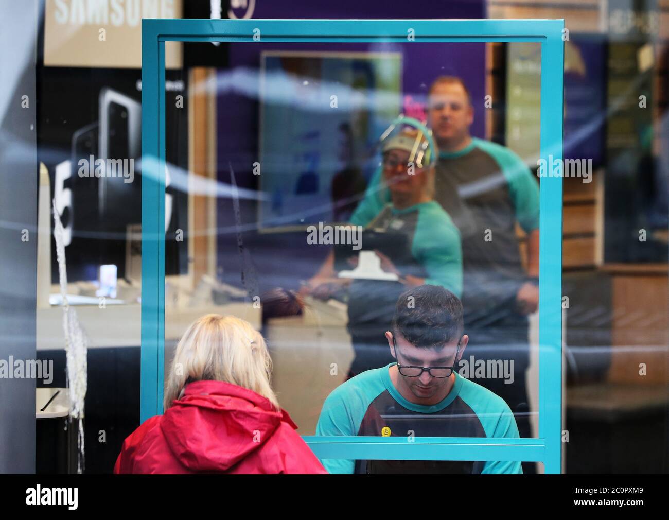 Un client parle avec un membre du personnel derrière une barrière de protection en verre plexiglas dans un magasin de Belfast après que tous les centres commerciaux et les détaillants ont reçu le feu vert pour rouvrir dans un assouplissement significatif des restrictions de blocage du coronavirus en Irlande du Nord. Banque D'Images