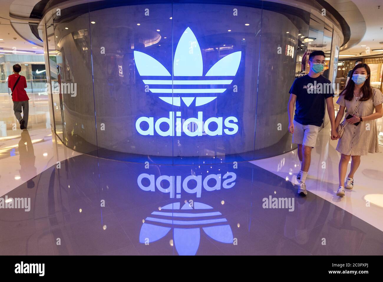 Les acheteurs portant des masques faciaux se promène devant le logo Adidas, une marque multinationale allemande de vêtements de sport, dans un centre commercial de Hong Kong Banque D'Images