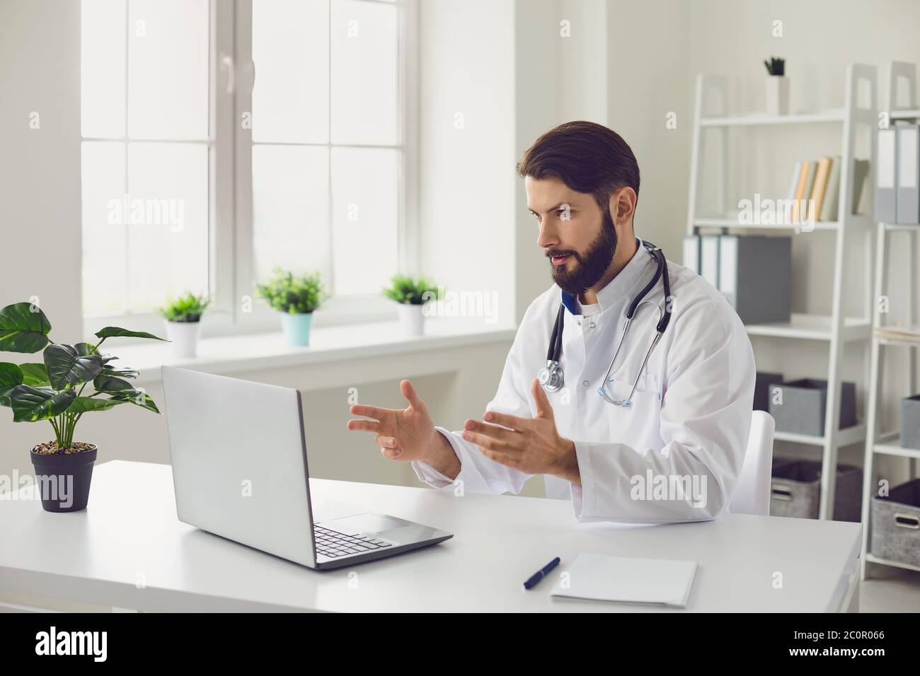 Médecin de sexe masculin fournissant une consultation médicale par vidéoconférence à l'aide d'un ordinateur portable au bureau. Banque D'Images