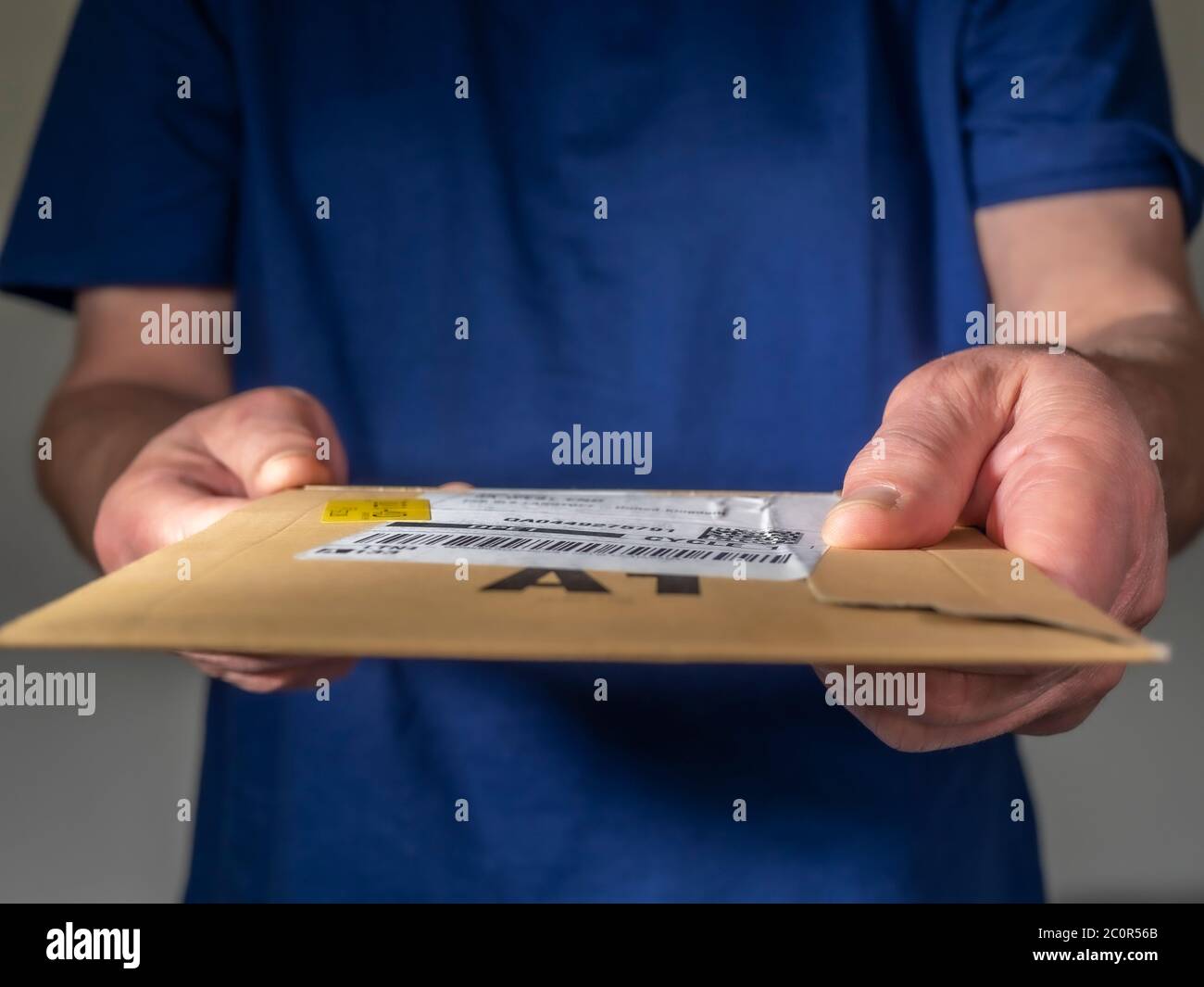 Homme dans un t-shirt bleu livrant un petit paquet, en remettant un paquet de carton plat avec l'étiquette de la compagnie d'expédition / de messagerie / de livraison. Banque D'Images