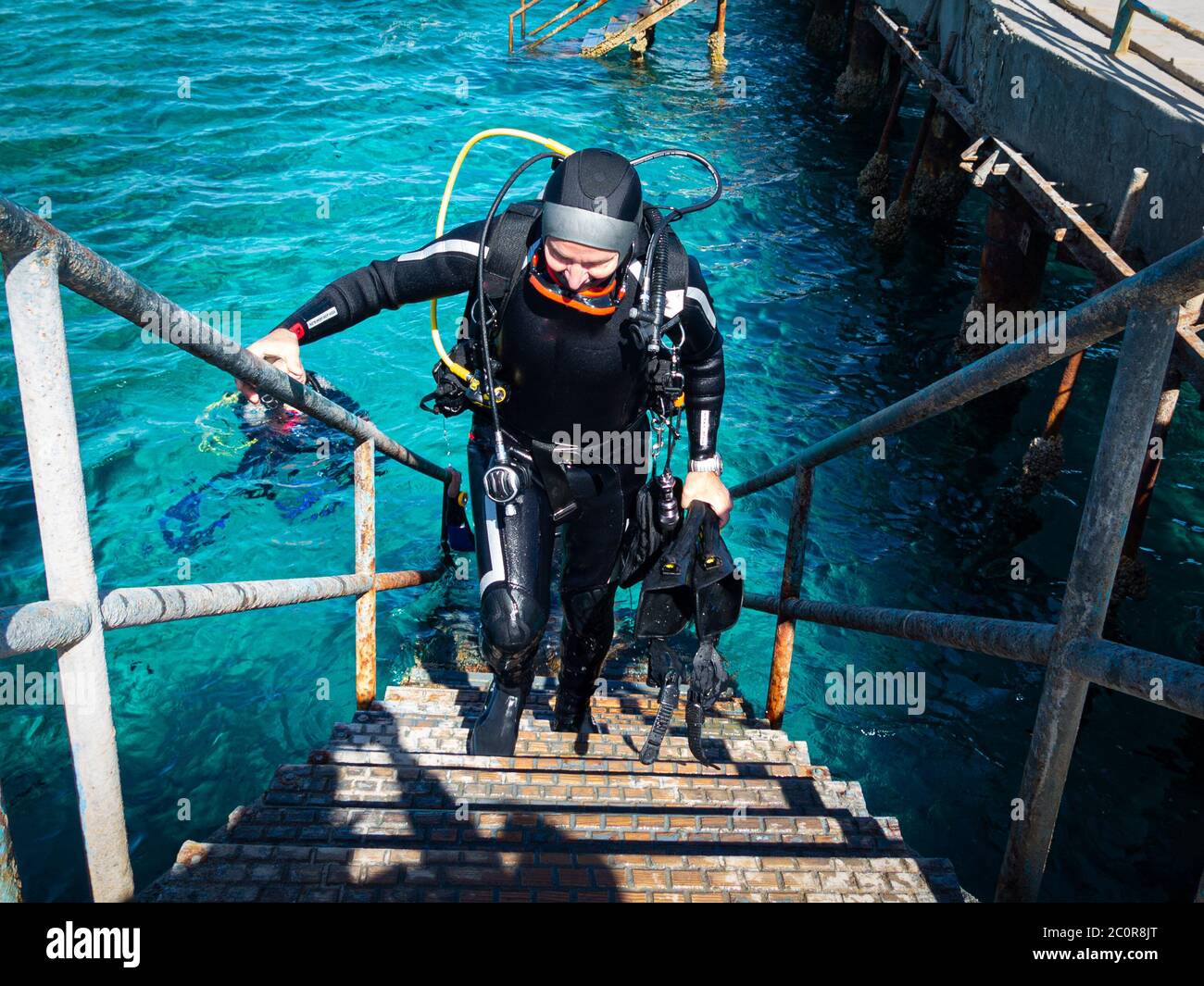 Un plongeur de plongée monte dans les escaliers jusqu'à la jetée, revenant d'une plongée sous-marine avec de l'équipement lourd sur son dos Banque D'Images