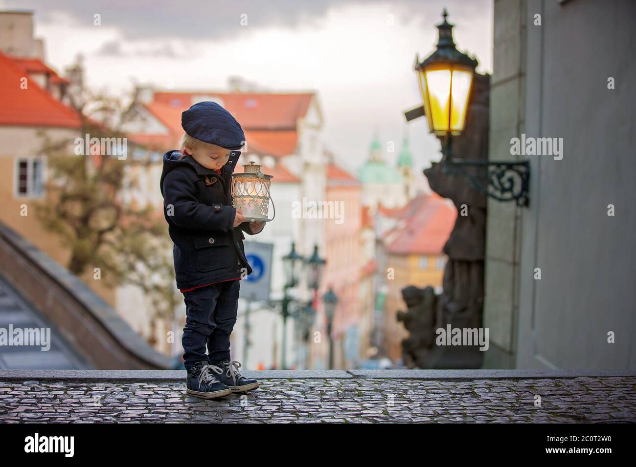 Magnifique enfant avec lanterne et ours en peluche, habillé à la mode, regardant la vue de nuit de Prague ville, l'hiver Banque D'Images