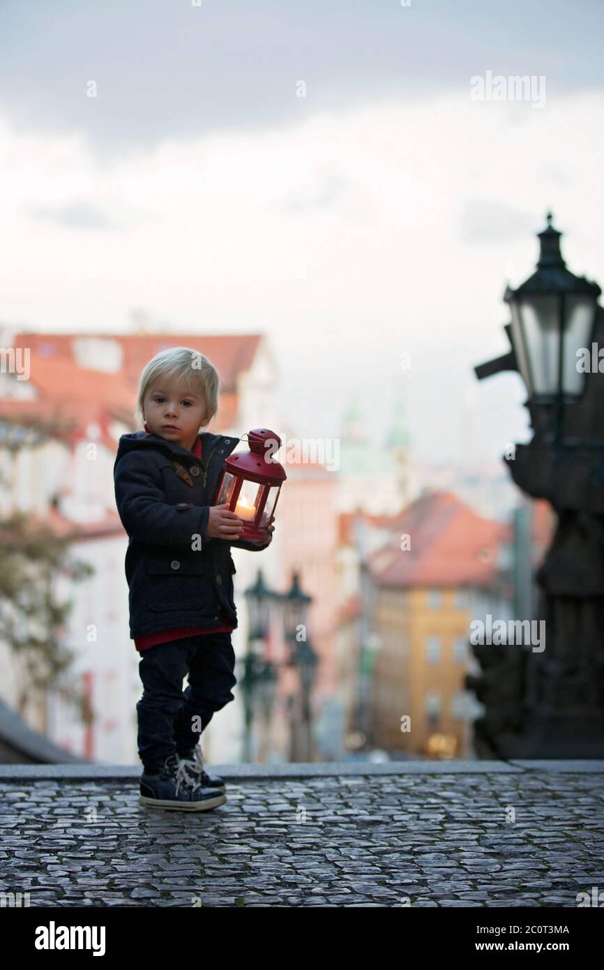 Magnifique enfant avec lanterne et ours en peluche, habillé à la mode, regardant la vue de nuit de Prague ville, l'hiver Banque D'Images