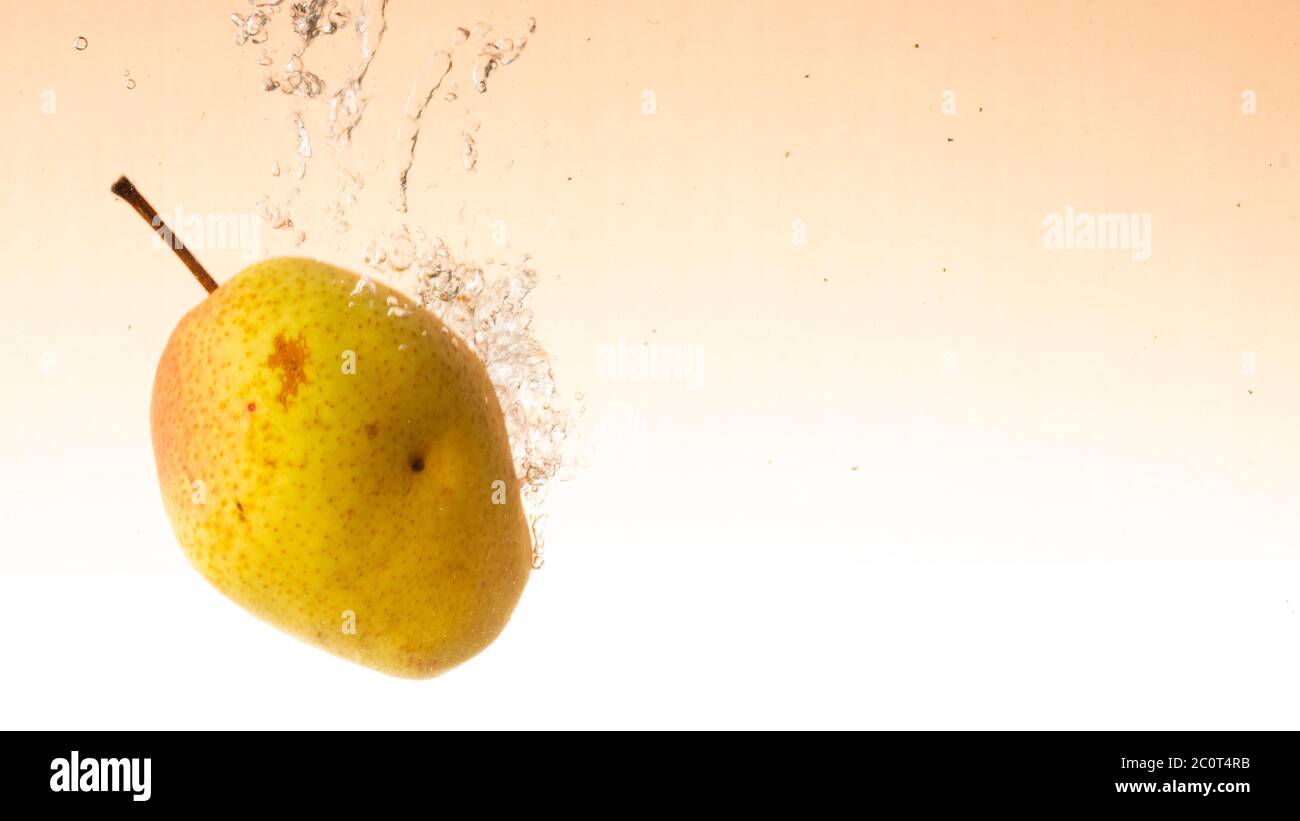 La poire fraîche avec des côtés vert-rouge tombe dans l'eau cognant des éclaboussures Banque D'Images