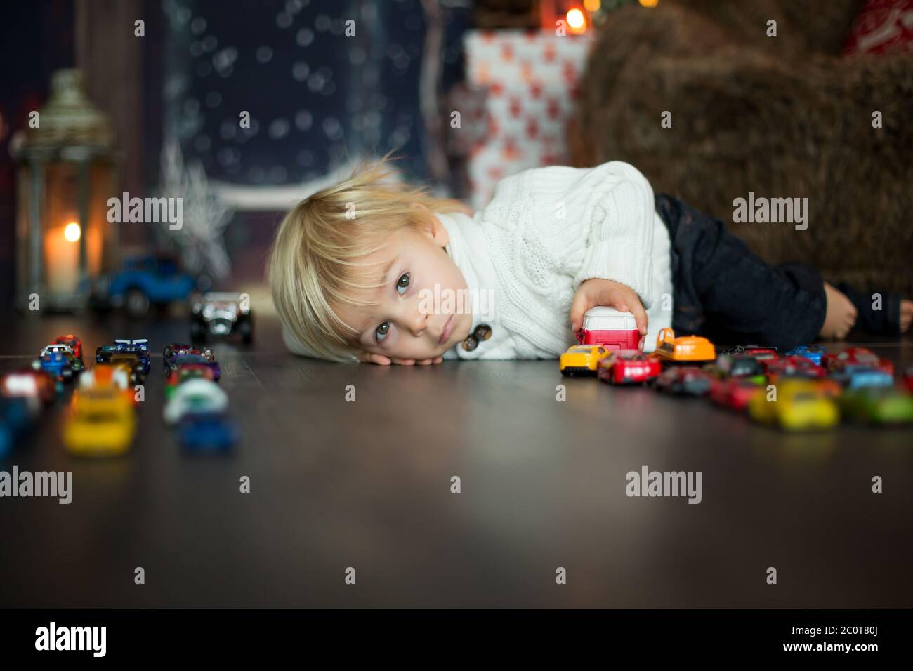 Un adorable petit garçon, assis autour de nombreux jouets de voiture sur le sol, jouant à Noël Banque D'Images