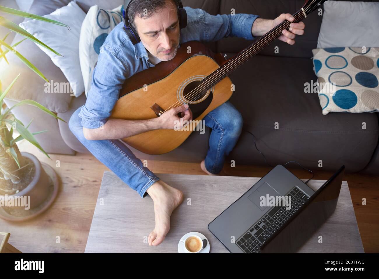 Homme écoutant de la musique avec un casque et jouant de la guitare regardant un ordinateur portable en même temps dans le salon à la maison. Vue de dessus Banque D'Images