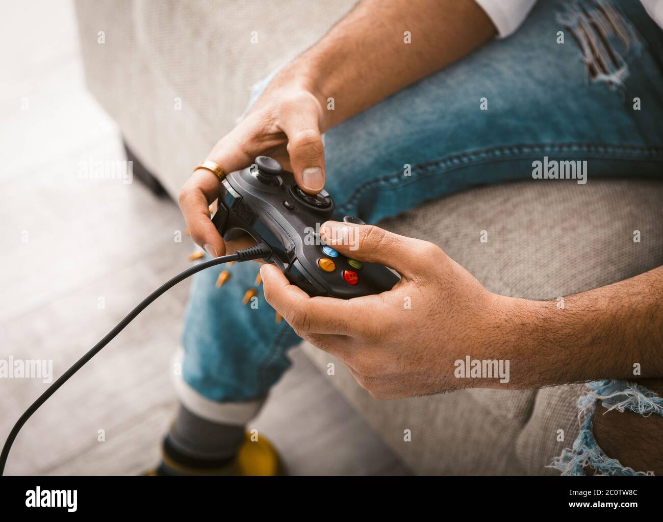 Utilisez le joystick pour faire la beauté des mains d'hommes. Le joueur utilise une manette de jeu filaire pour jouer à des jeux informatiques. Gros plan. Concept Home Entertainment. Image en tons Banque D'Images