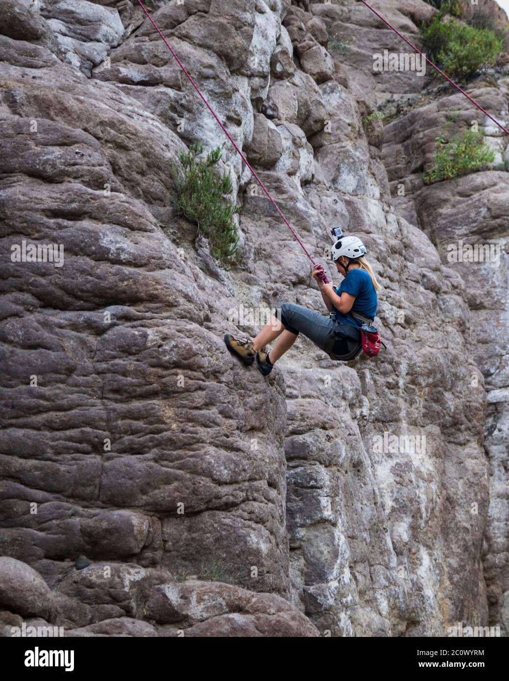 femme grimpant sur une montagne rocheuse, avec harnais et casque Banque D'Images