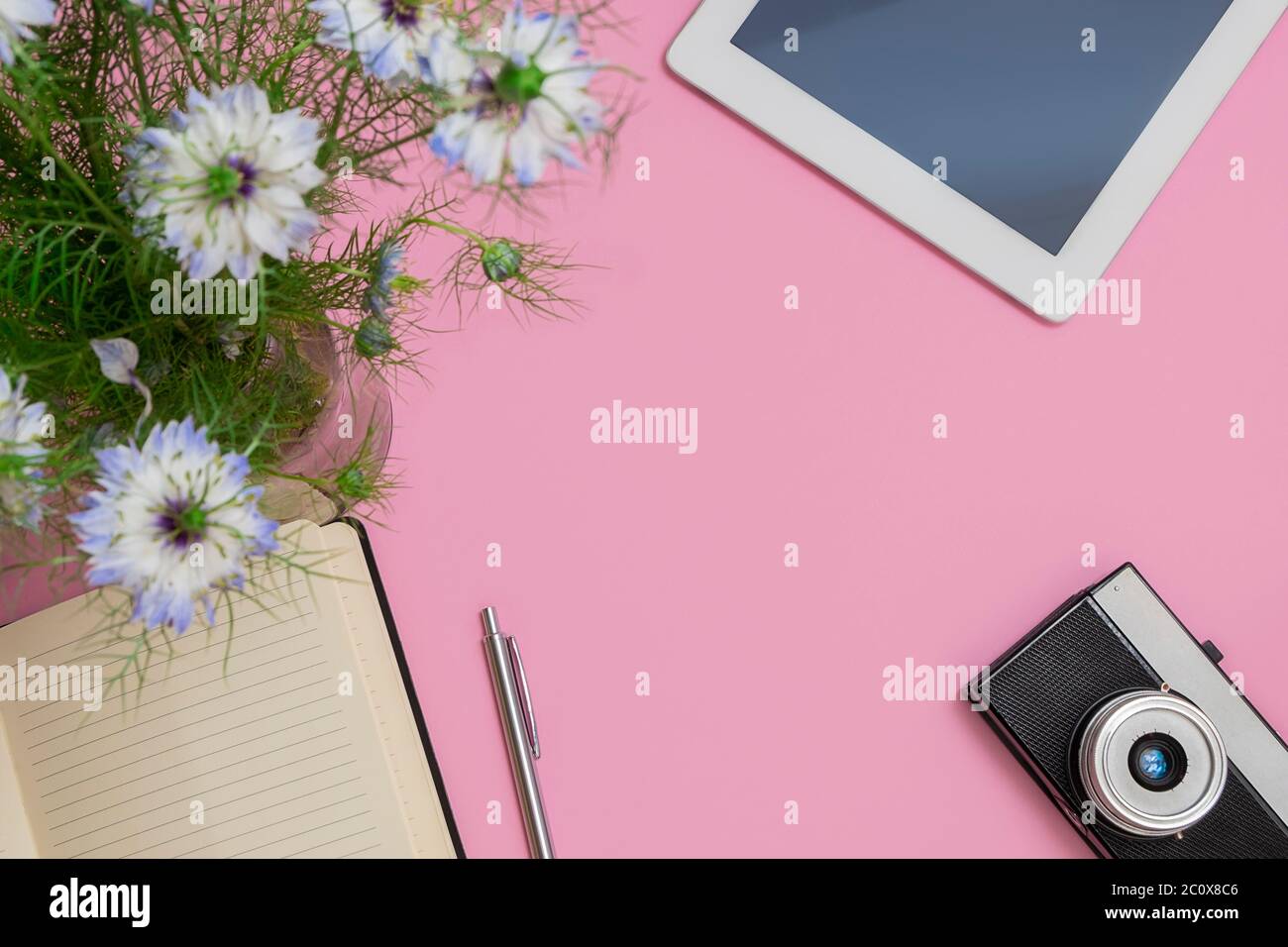 Vue de dessus d'un espace de travail de blogueur ou de freelance avec tablette, fleurs, bloc-notes, stylo, appareil photo sur fond rose pastel avec espace de copie Banque D'Images