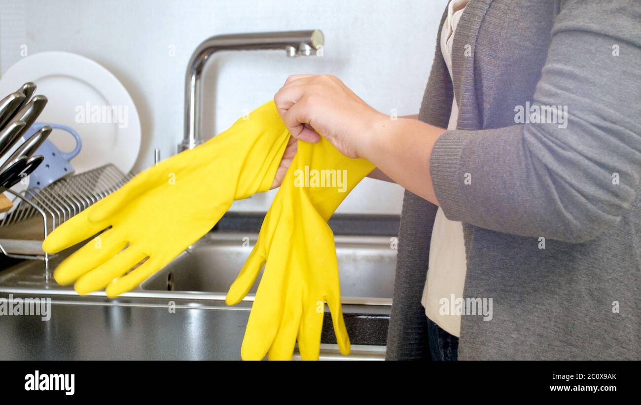 Jeune femme au foyer se protégeant les mains avec des gants en caoutchouc jaune avant de faire des travaux à la maison Banque D'Images