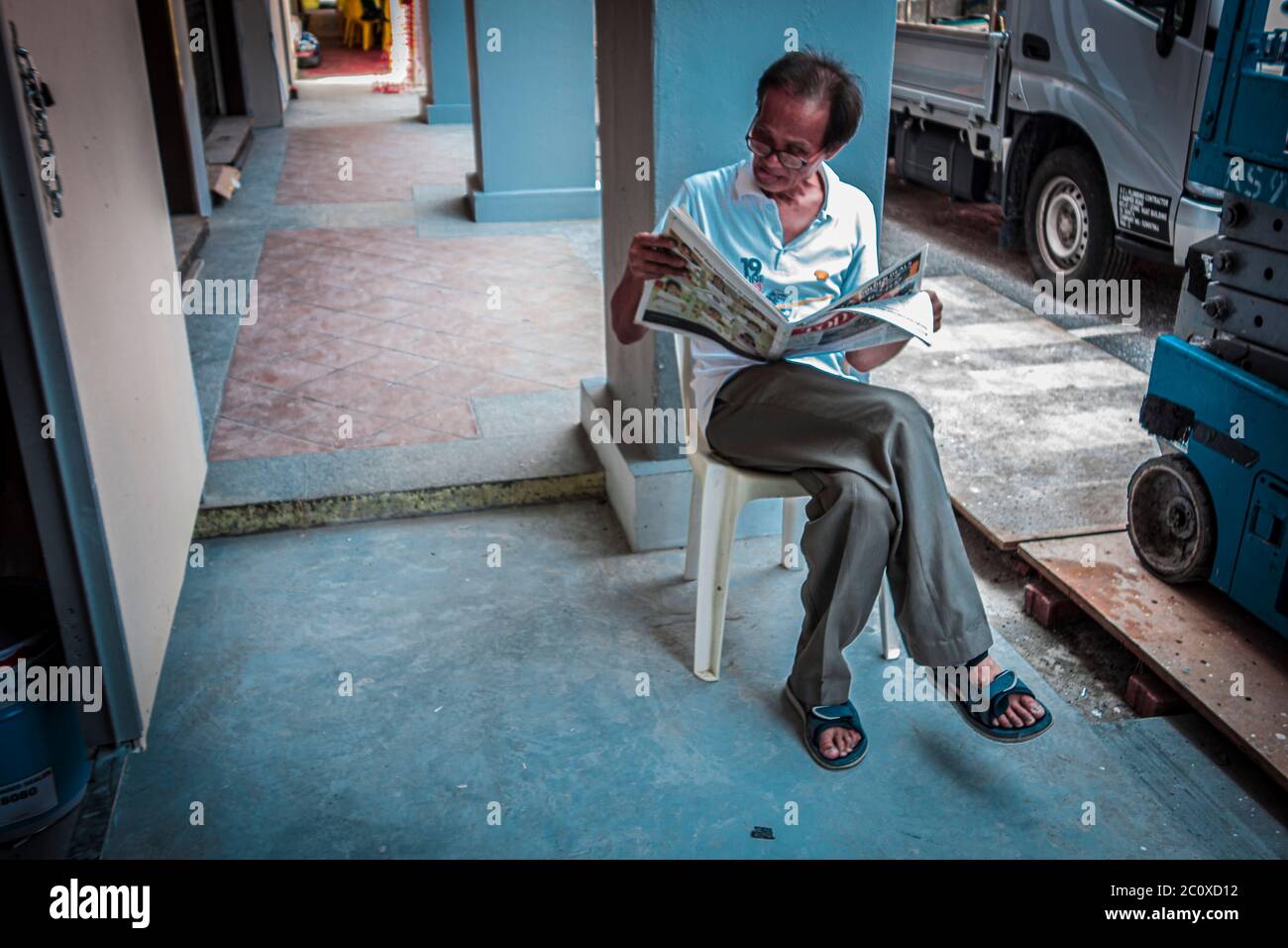 Scène de rue d'un homme lisant un journal assis sur une chaise en plastique. Buffalo Road. Petite Inde. Singapour Banque D'Images