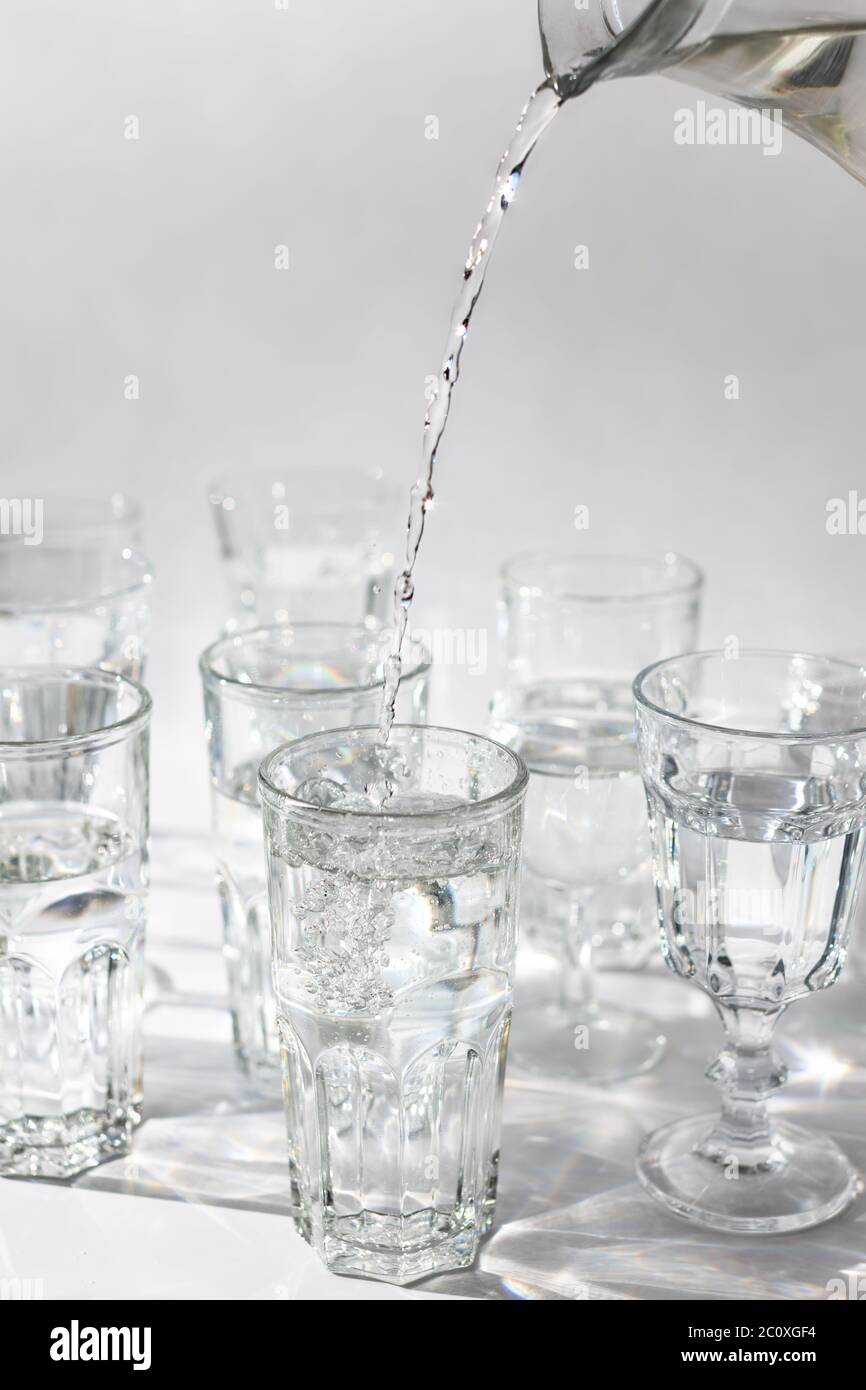 La main verse de l'eau fraîche d'un décanter dans un fond en verre, clair. Gros plan, vertical. Banque D'Images