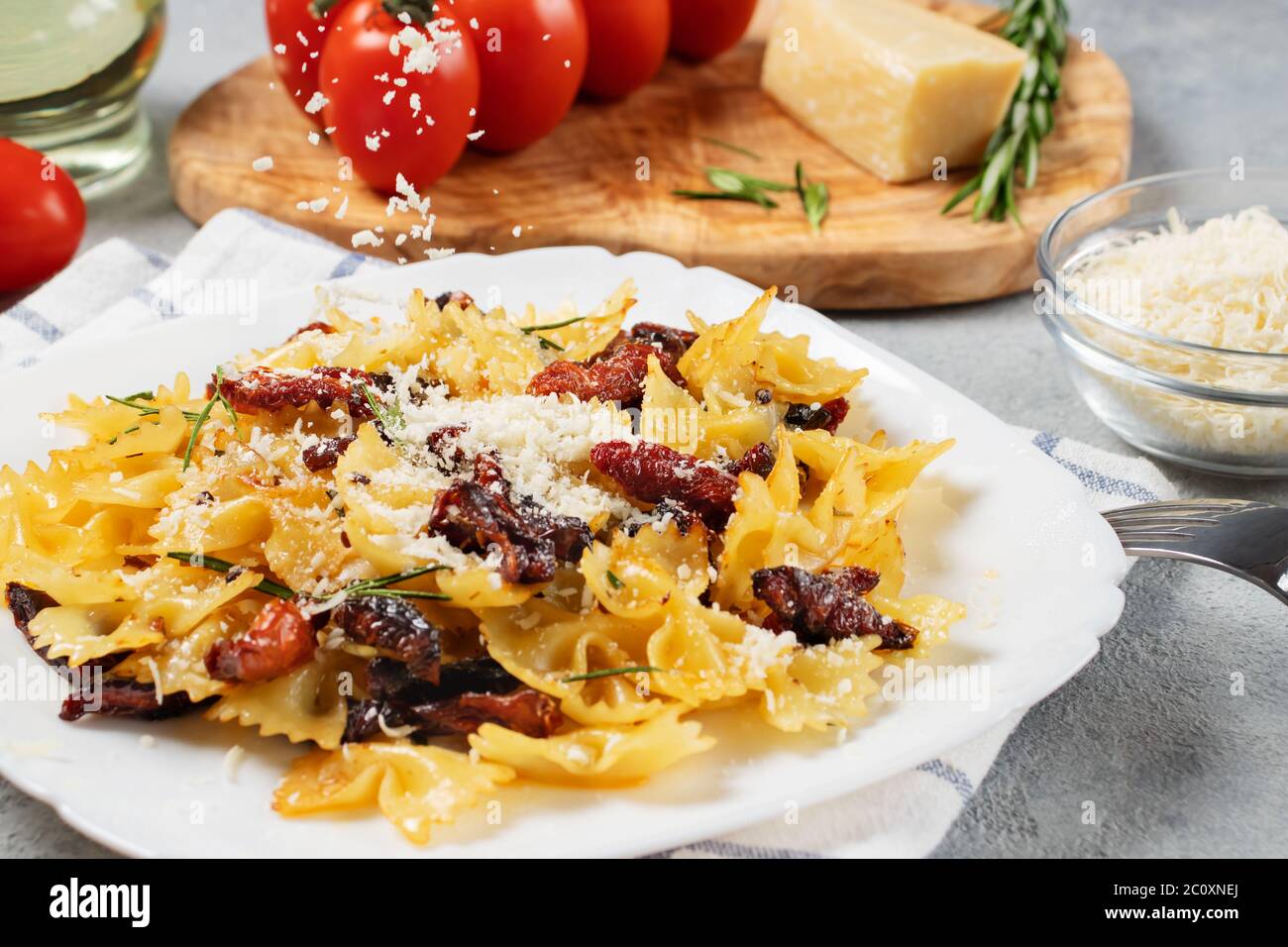 Saupoudrer les pâtes au parmesan avec des tomates séchées dans une assiette blanche sur la table. Cuisine italienne, ingrédients et plat fini. Banque D'Images
