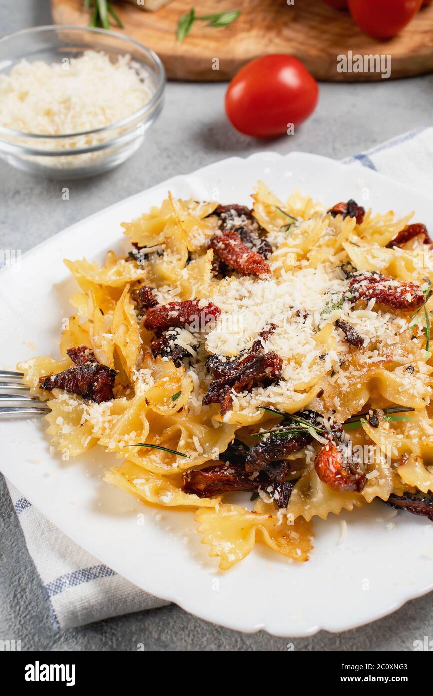 Pâtes avec tomates séchées et parmesan dans une assiette blanche sur la table. Plat alimentaire italien, image verticale. Banque D'Images