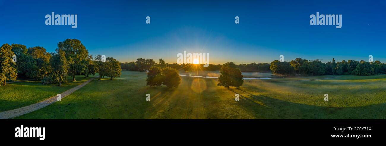 Magnifique panorama du jardin anglais à Munich, bavière, allemagne. Le brouillard se lève tôt tandis que le soleil brille à travers deux arbres verts. Mystique Banque D'Images