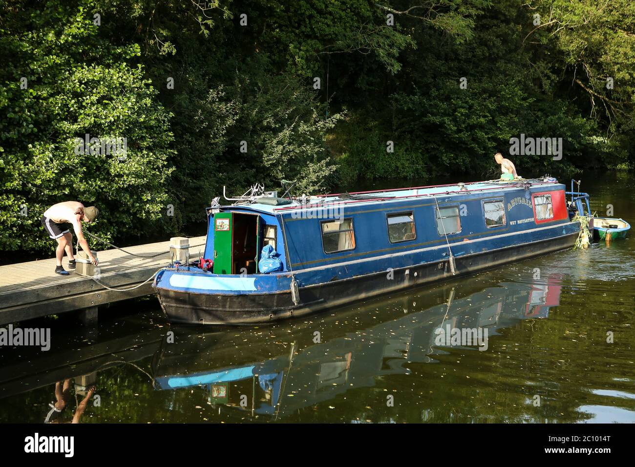 Deux hommes amarent un bateau bleu étroit sur une jetée sur la rivière Medway près de Hadlow, dans le Kent Banque D'Images