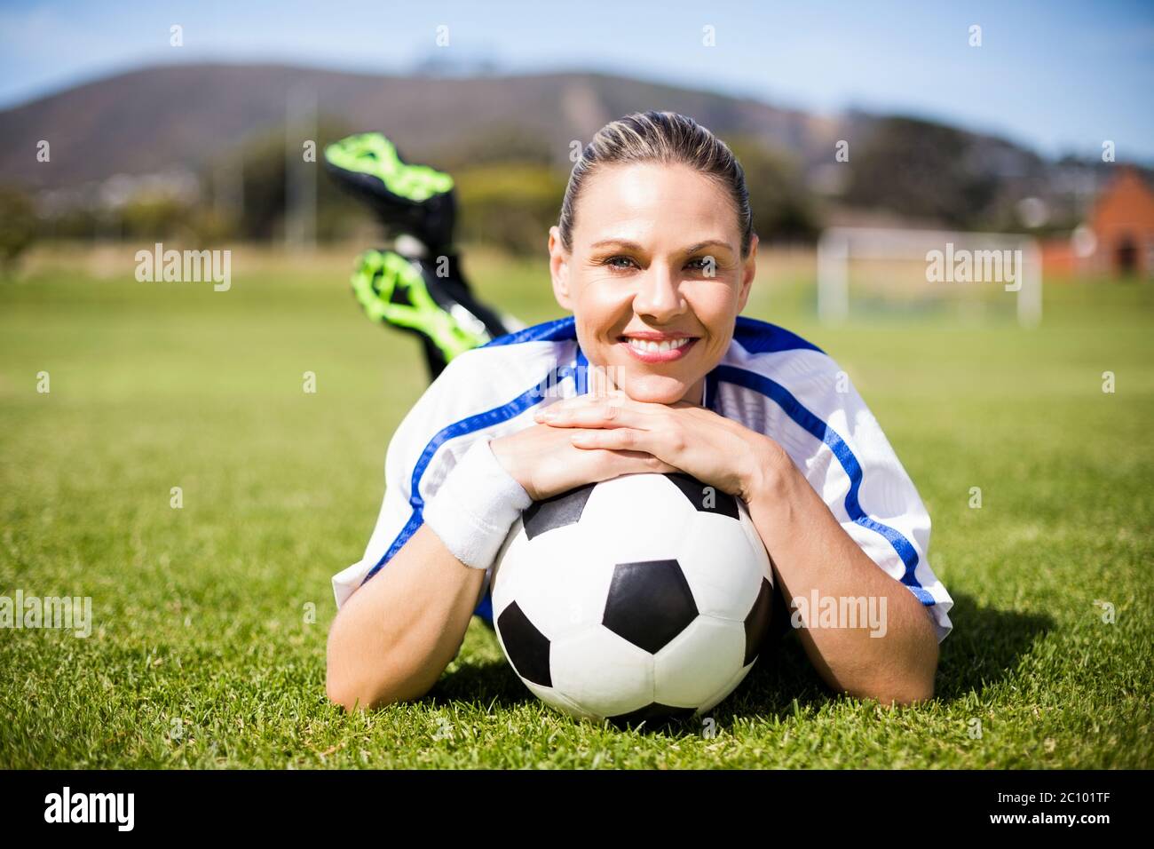 Portrait de joueur de football féminin allongé sur terrain de football avec ballon Banque D'Images