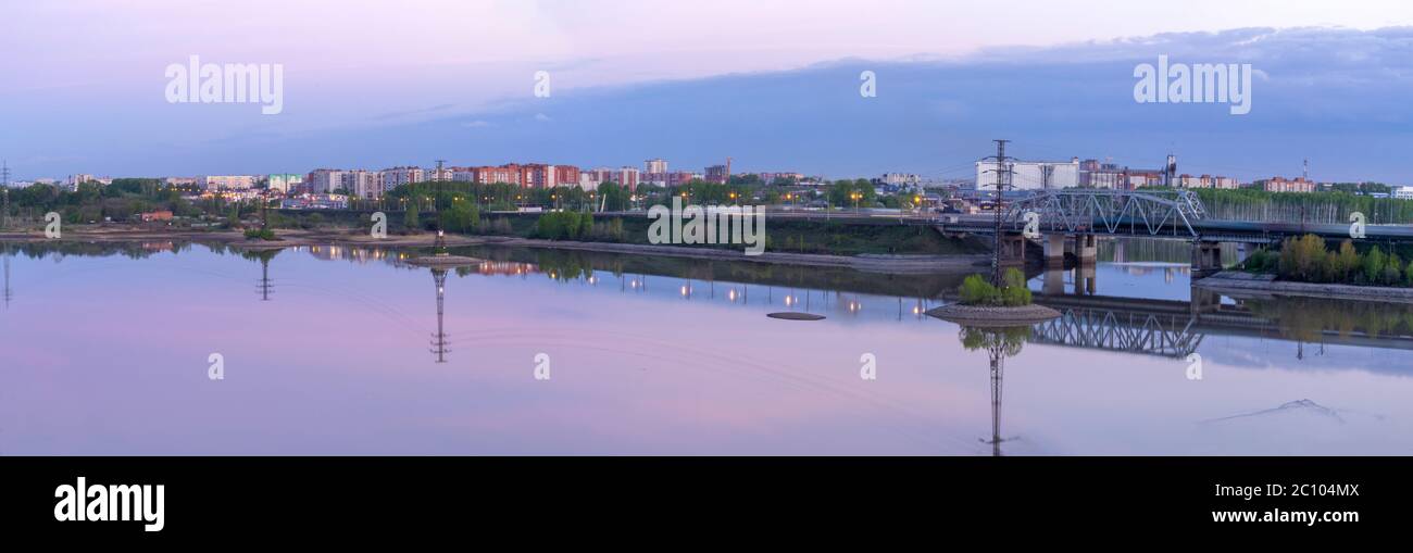 Panorama de la ville du soir. Le pont ferroviaire se reflète dans l'eau. Il y a des nuages dans le ciel Banque D'Images