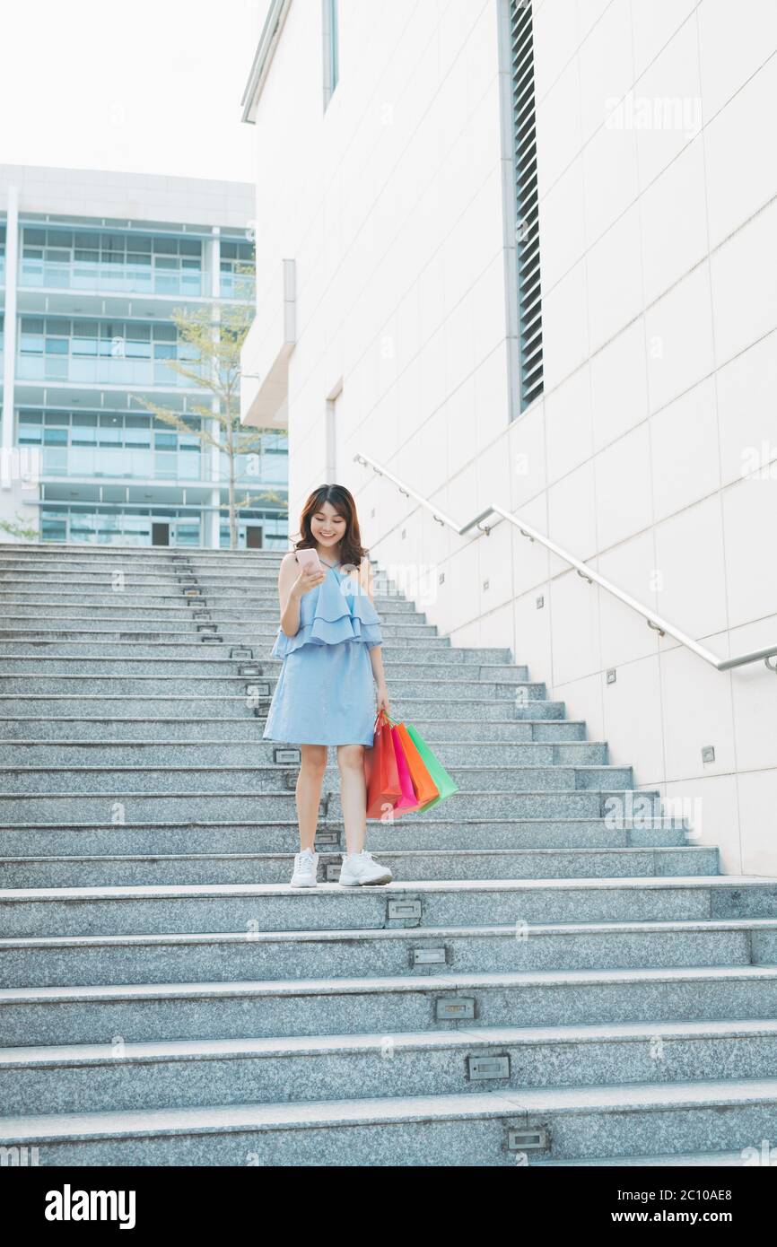 Jeune femme asiatique descendant les escaliers et tenant des sacs à provisions dans la main, concept de shopping Banque D'Images