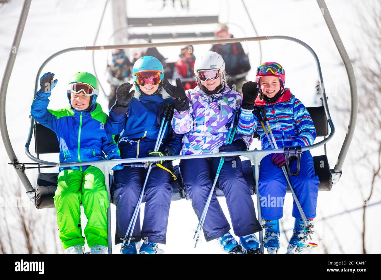 Un groupe de quatre enfants s'assoient sur le télésiège et se branchient à la montagne sur la station de ski alpin Banque D'Images