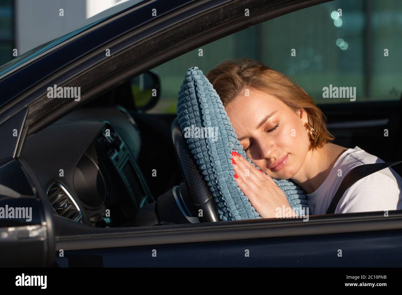 Jeune femme fatiguée conducteur endormi sur l'oreiller sur le volant, se reposant après de longues heures de conduite d'une voiture. Fatigue. Privation de sommeil. Banque D'Images