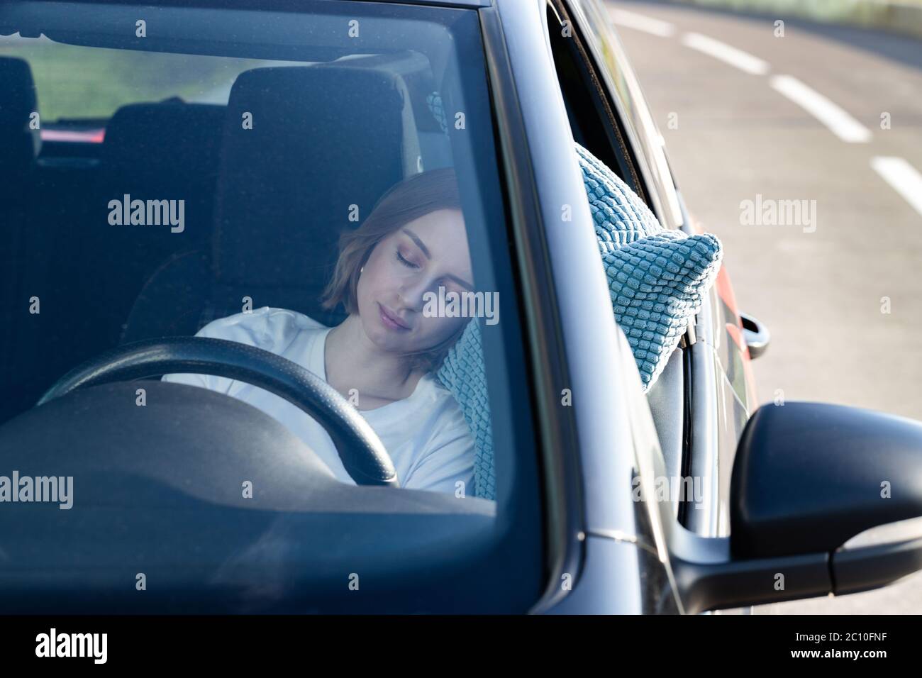 Jeune femme fatiguée conducteur endormi sur l'oreiller sur le volant, se reposant après de longues heures de conduite d'une voiture. Fatigue. Privation de sommeil. Banque D'Images