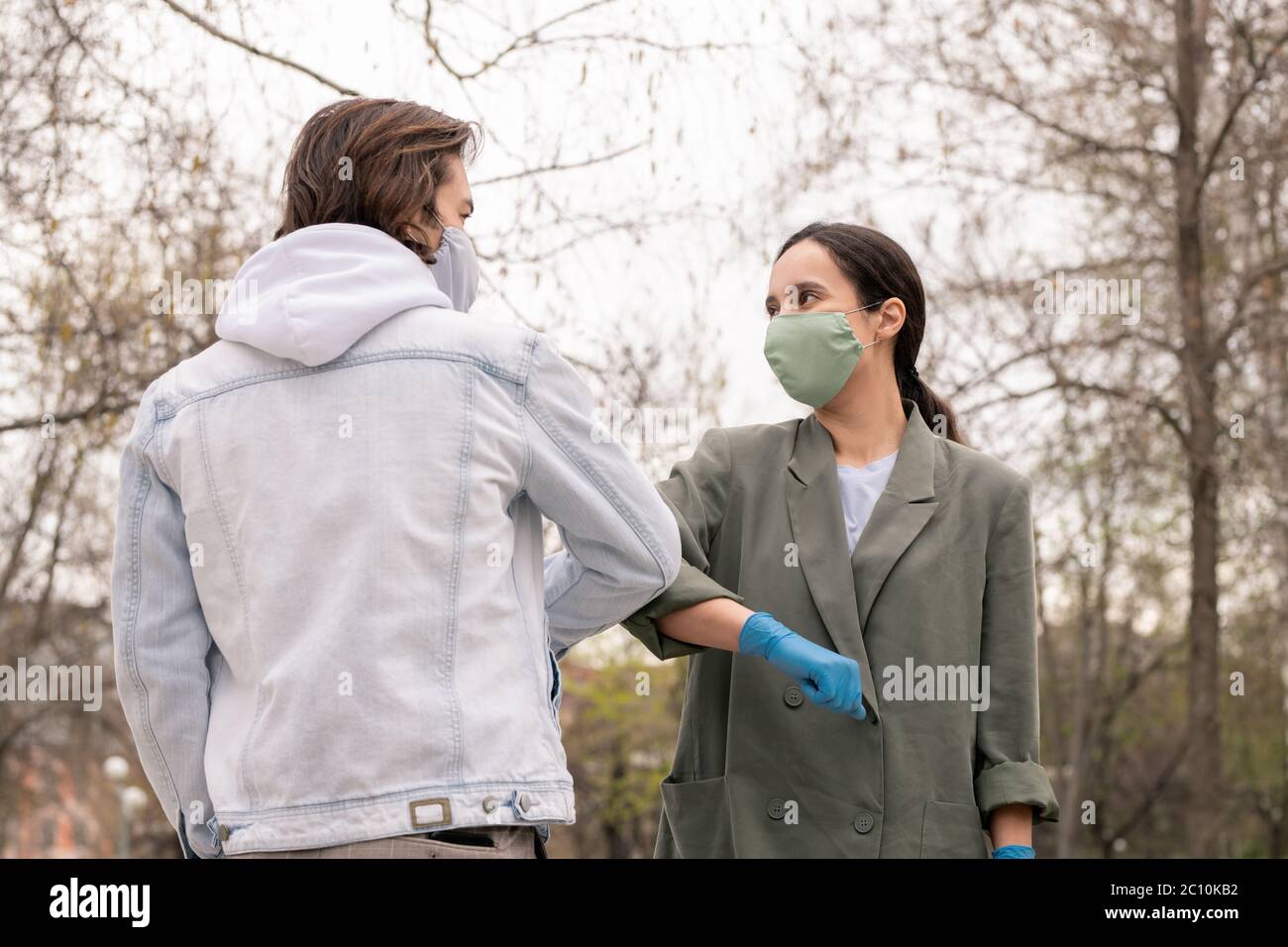 Jeune beau couple dans les masques protecteurs saluant l'un l'autre avec coude tactile geste dans le parc Banque D'Images