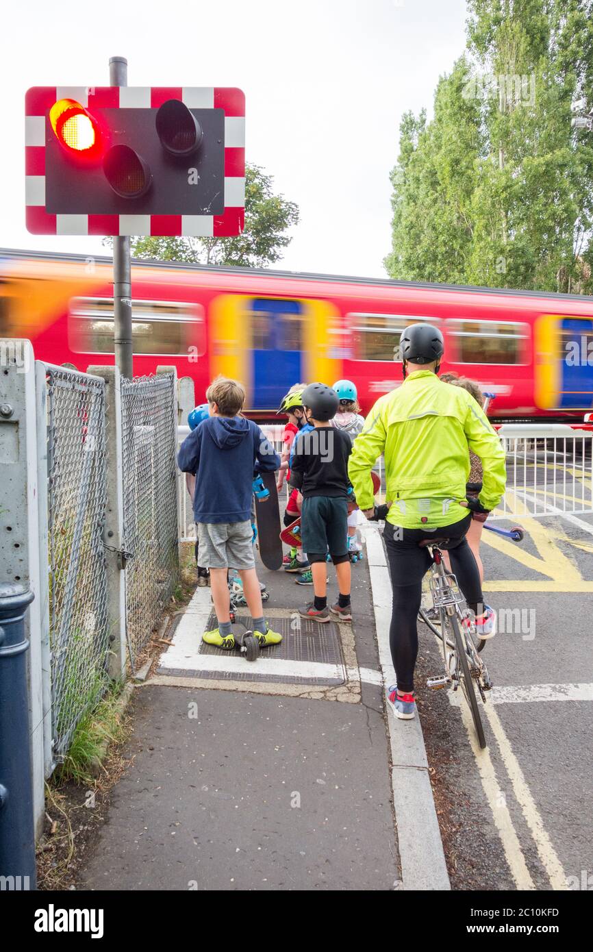 Un cycliste et un groupe de jeunes enfants attendent au passage à niveau de la route Vine de Network Rail à Barnes, SW London, Royaume-Uni Banque D'Images