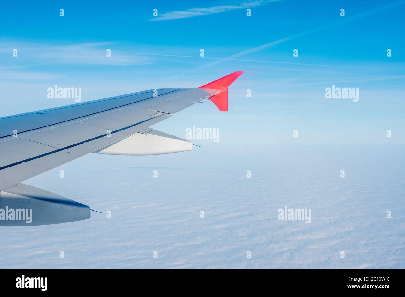 Aile d'avion contre le fond du ciel bleu clair et de la mer de nuages blancs denses en dessous. Banque D'Images