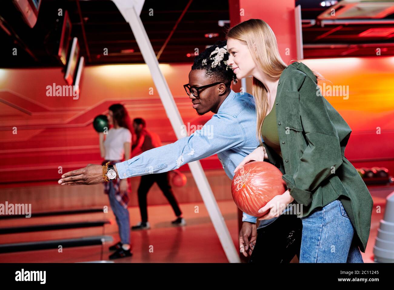 Un jeune homme d'origine africaine qui pointe sur la piste de bowling tout en expliquant à sa petite amie comment lancer le ballon pour frapper toutes les quilles Banque D'Images