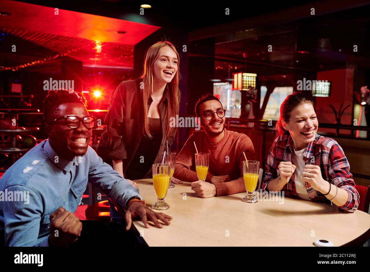 Jeunes fans de diverses origines ethniques et joyeux qui regardent la diffusion de leur équipe de bowling préférée tout en étant assis à table et en prenant un verre Banque D'Images