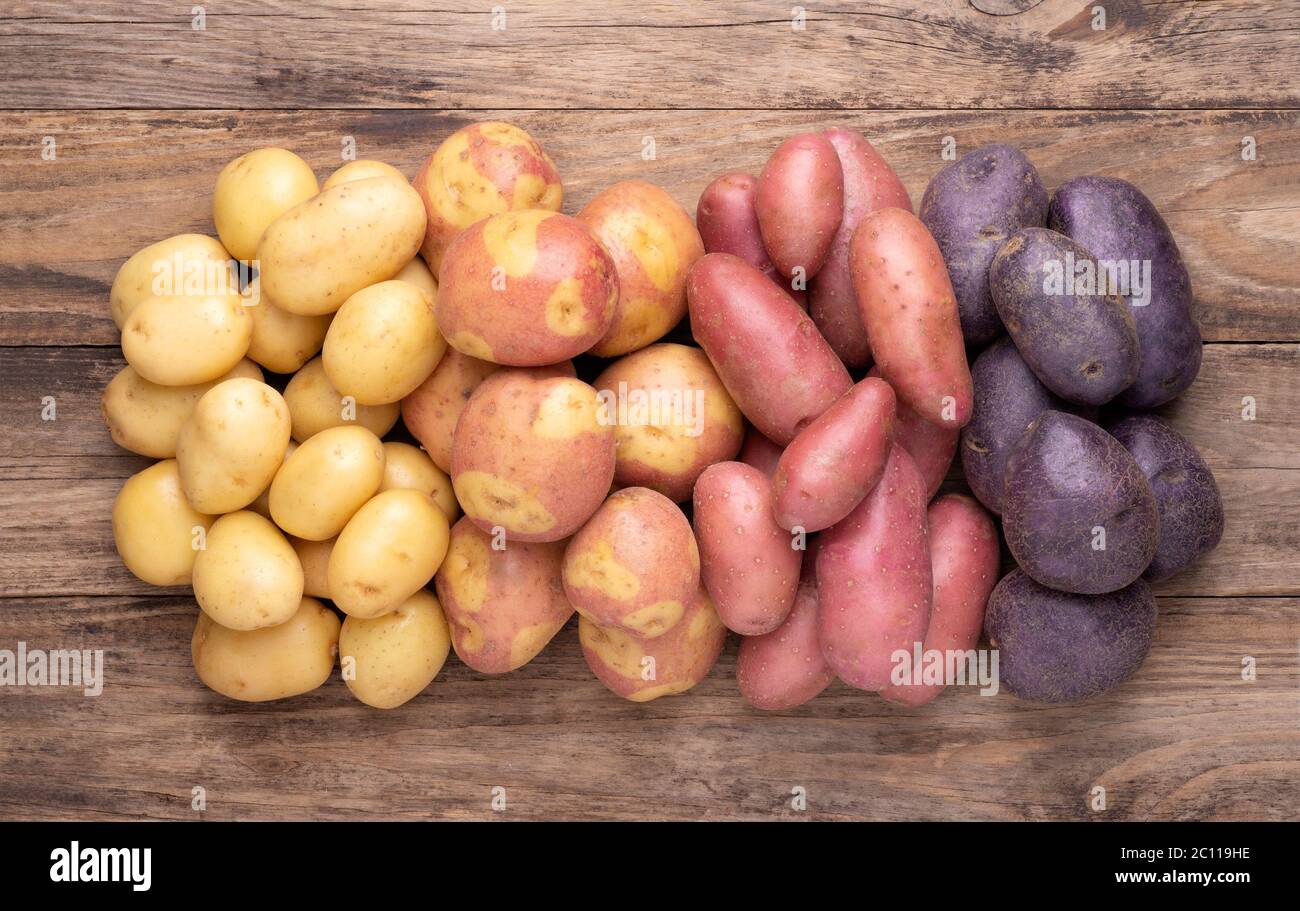 Tas de différents types de pommes de terre sur table rustique en bois Banque D'Images